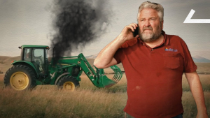 Man talking on a phone witha green tractor behind him