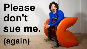 A man sitting on an orange 3D-printed designer chair with text reading 'Please don’t sue me (again),' showcasing a unique DIY creation.